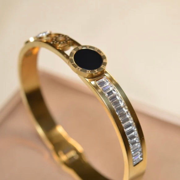 Gold bracelet with black center stone and diamond accents on a beige background