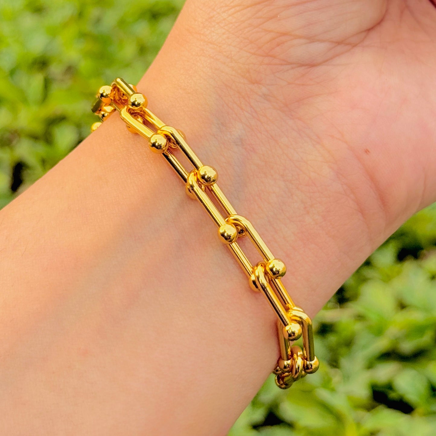 Gold bracelet on a wrist with a blurred green background