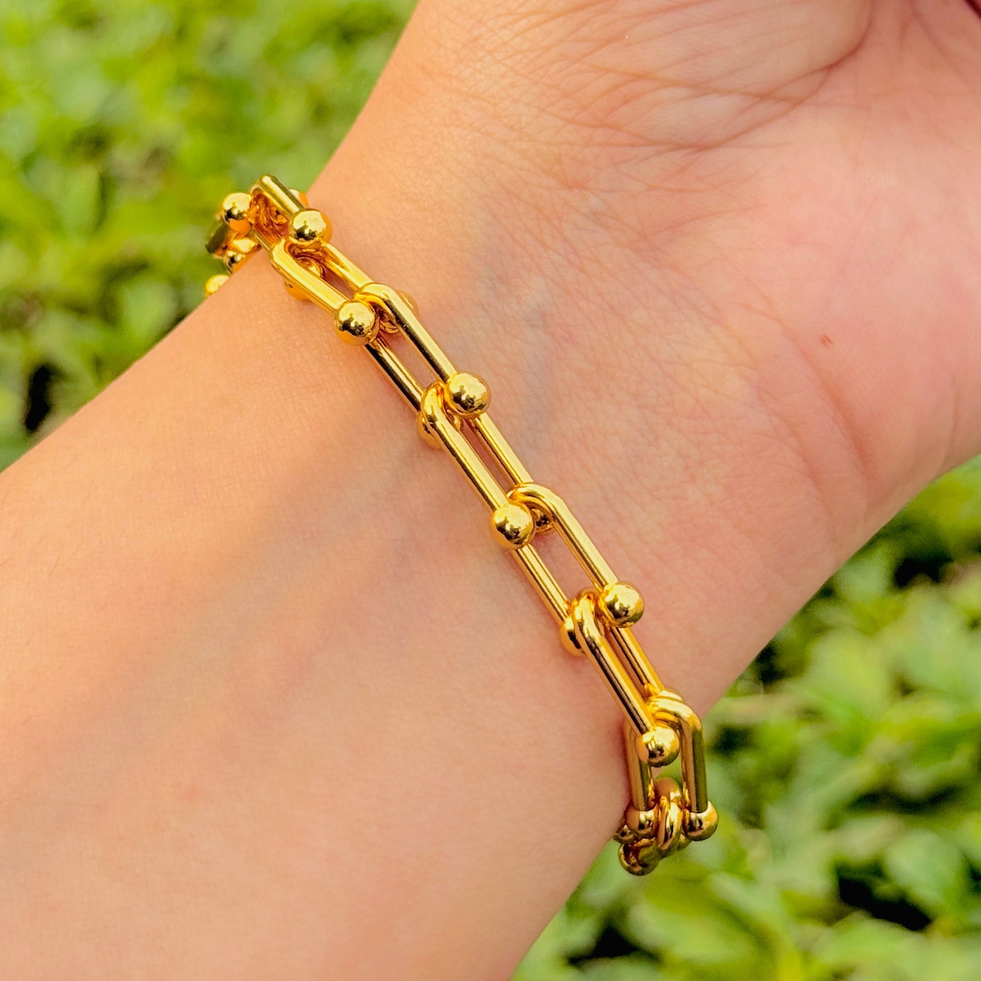 Gold bracelet on a wrist with a blurred green background