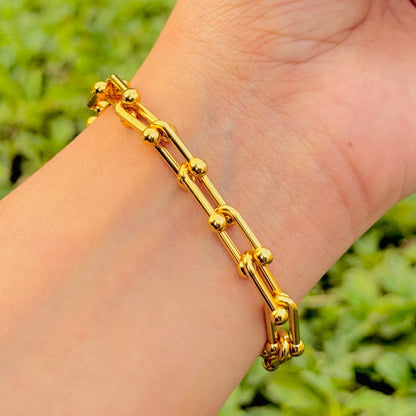 Gold bracelet on a wrist with a blurred green background