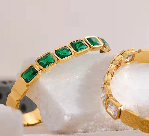 Gold bracelet with green gemstones on a white stone background