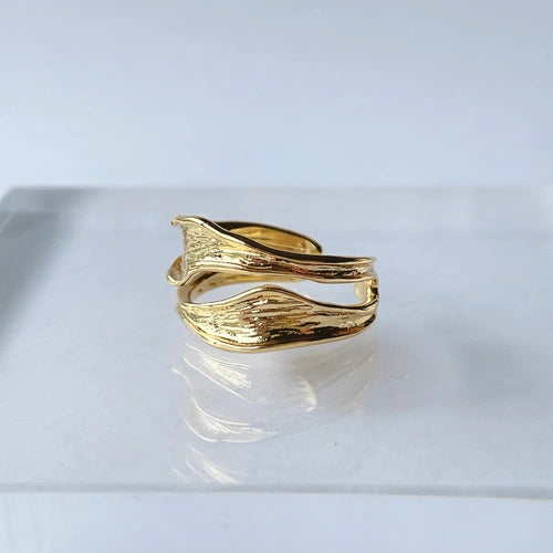 Gold ring with wavy design on a reflective surface