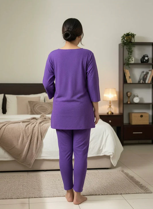 Woman in purple loungewear standing barefoot in bedroom near bed and bookshelves