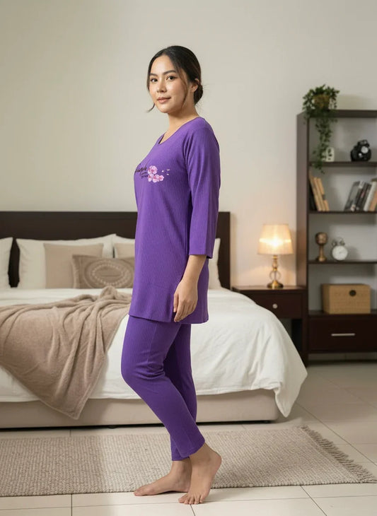 Woman in purple ribbed pajamas standing in modern bedroom with bed and bookshelf