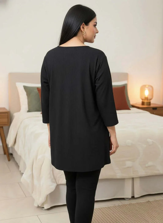 Woman in black long tunic and leggings standing in modern bedroom with cozy bed and lamp