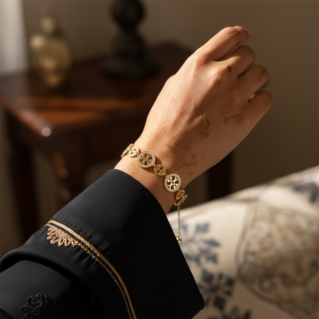 Hand wearing a gold bracelet with intricate designs, set against a blurred indoor background.