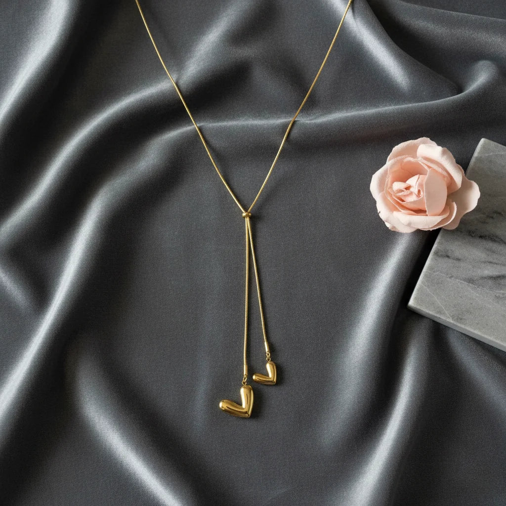 Gold necklace with heart-shaped pendants on a dark fabric background with a pink flower.