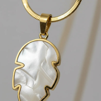 Gold necklace with a white pendant on a gray background
