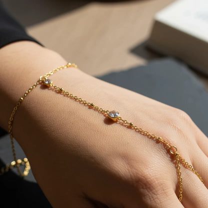 Gold bracelet with small stones on a wrist against a neutral background