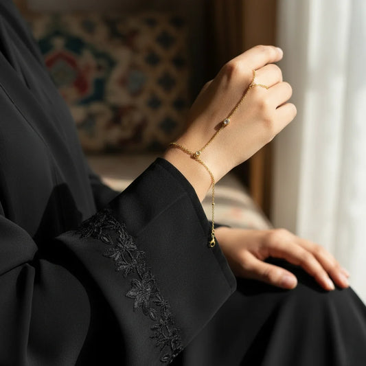 Person wearing a gold bracelet and ring, sitting in a softly lit room.