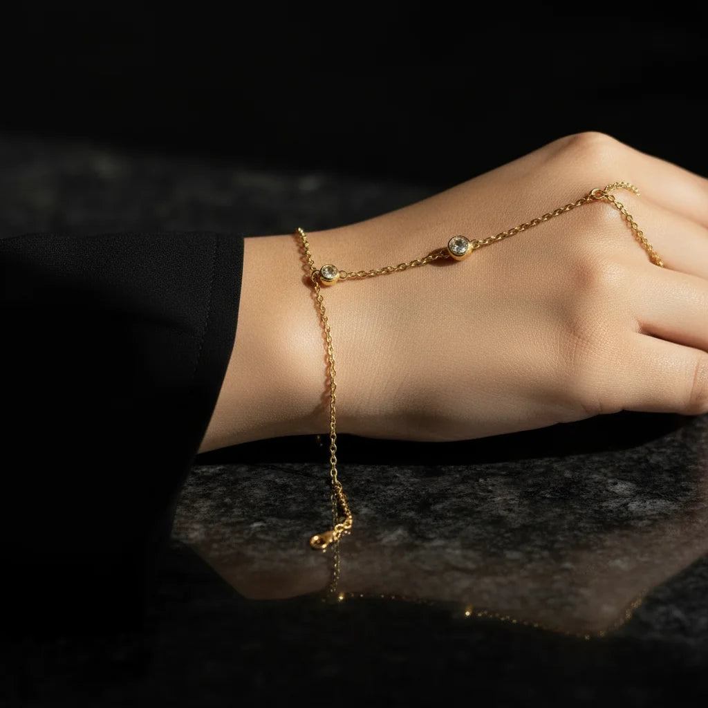 Gold anklet with small green stones on a person's ankle against a dark background