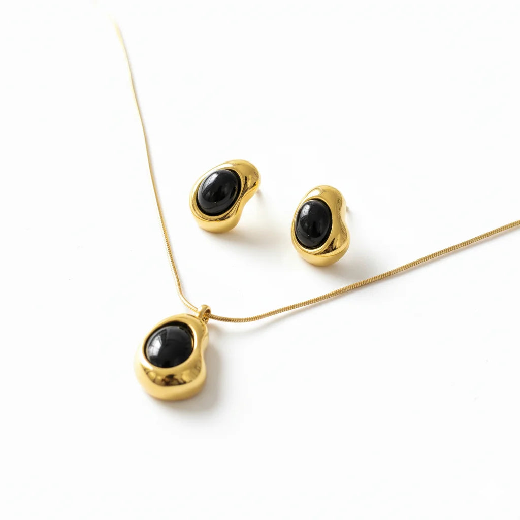 Gold necklace and earrings with black stones on a white background