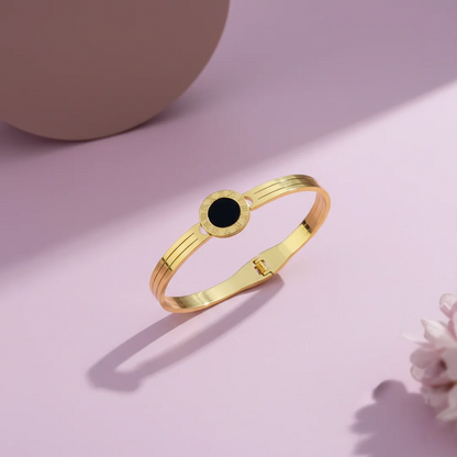 Gold bracelet with a black stone on a pink background