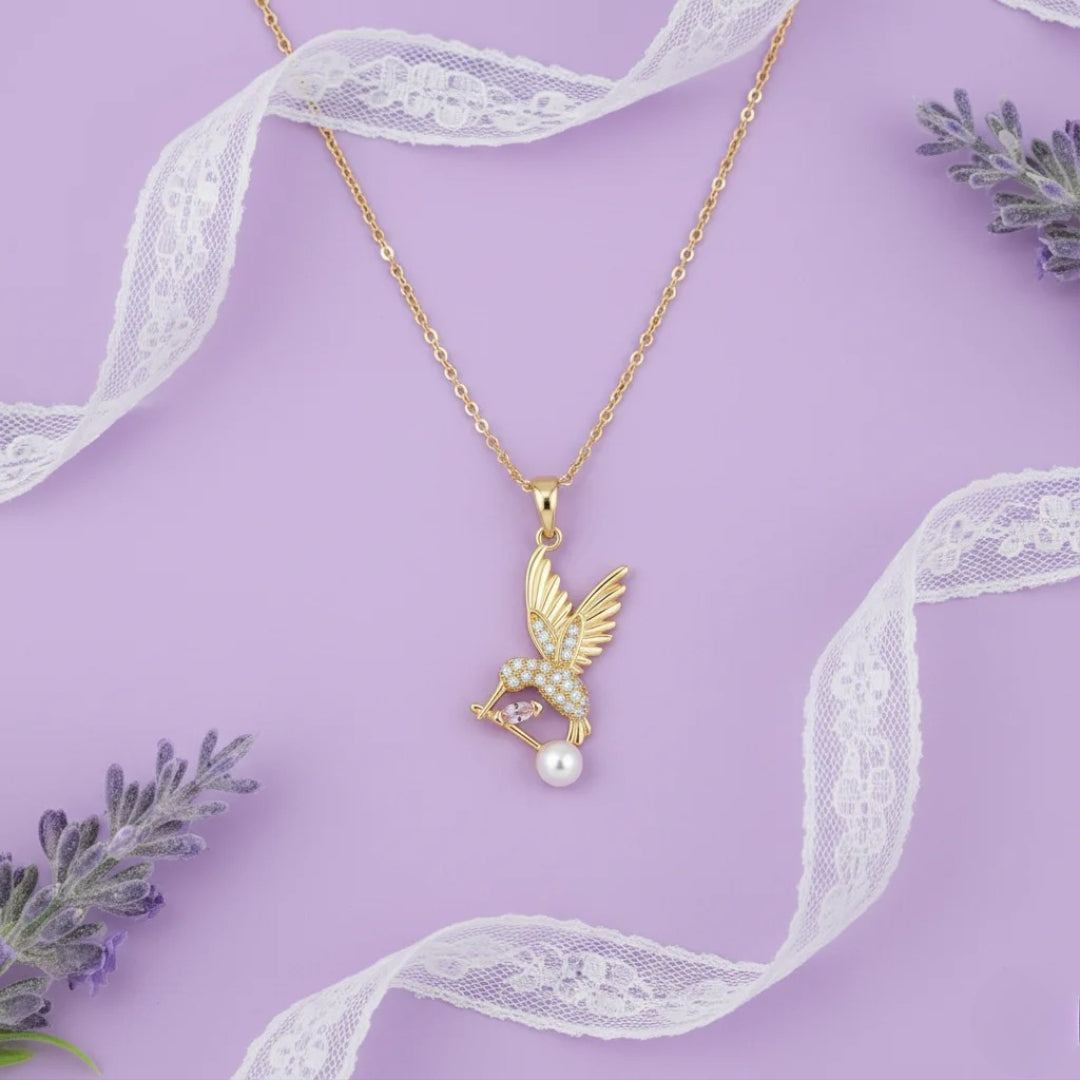 Gold necklace with a pendant featuring a pearl on a purple background with lace and lavender.