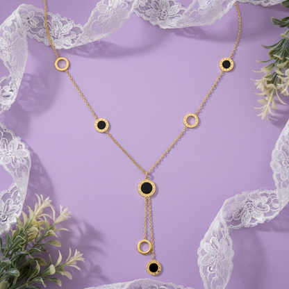 Gold necklace with black stones on a purple background with lace and greenery