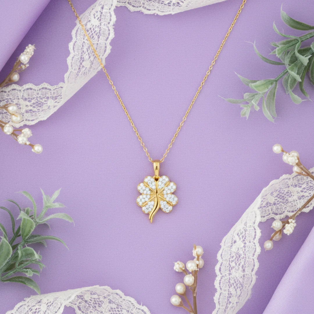 Gold necklace with a clover pendant on a purple background with lace and flowers.