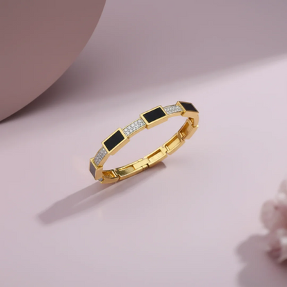 Gold bracelet with black and clear gemstones on a pink background