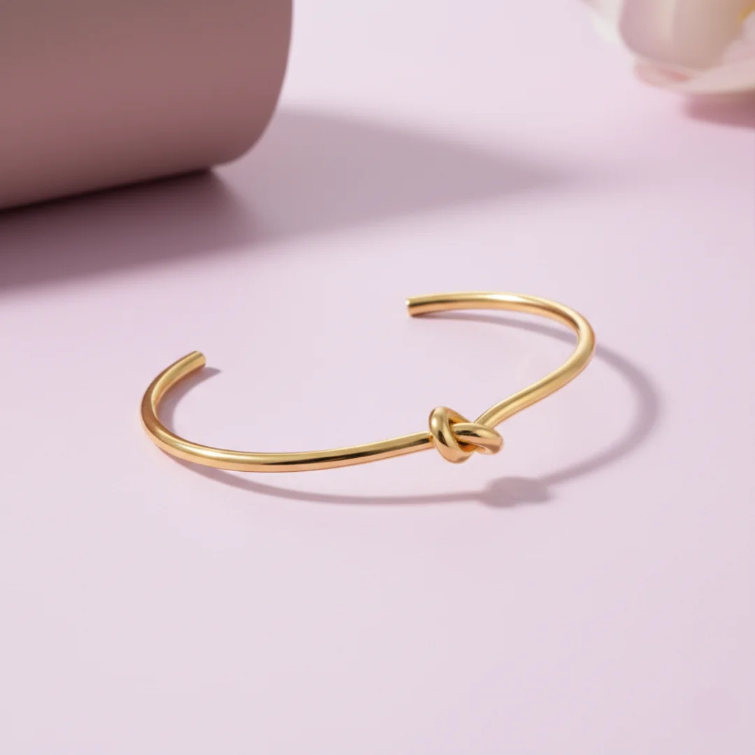 Gold bracelet with knot design on a pink background