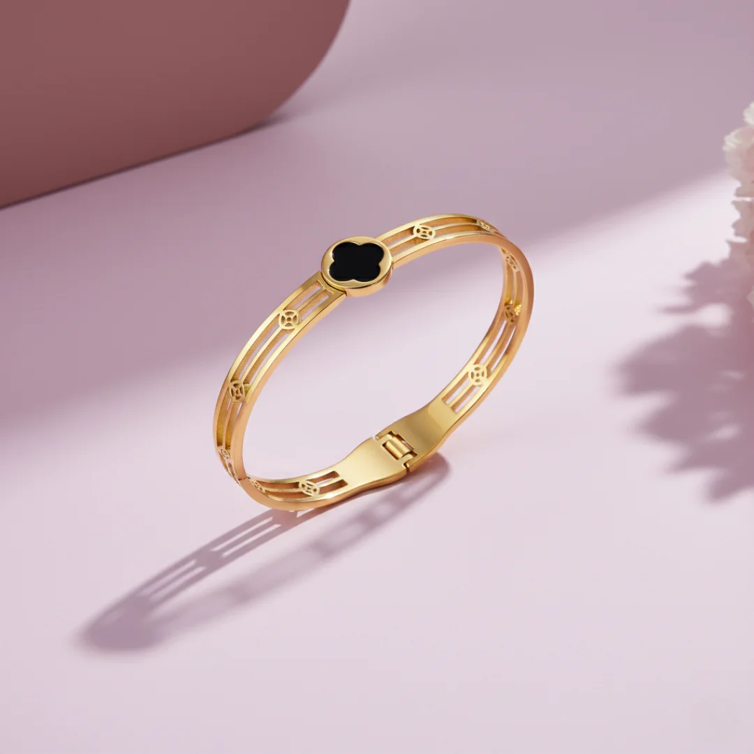 Gold bracelet with a black gemstone on a pink background