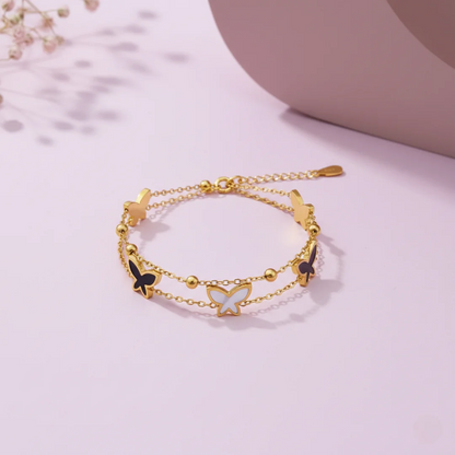 Gold bracelet with butterfly charms on a light pink background