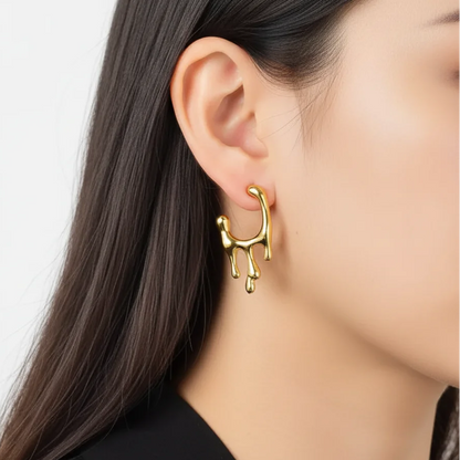 Gold earring worn by a person with a plain background