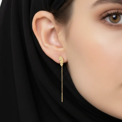 Close-up of a woman wearing gold earrings with a black hijab on a light gray background