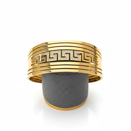 Gold bracelet with a geometric design on a gray stand against a white background