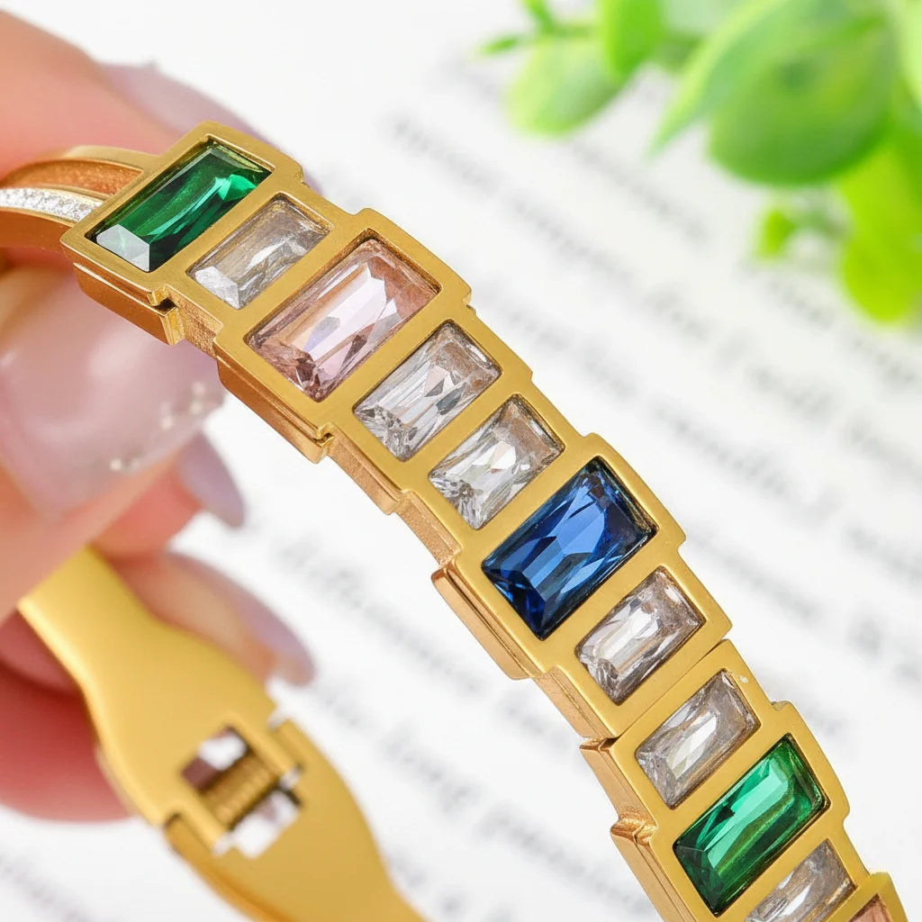 Gold bracelet with colorful gemstones held by a hand against a blurred green plant background