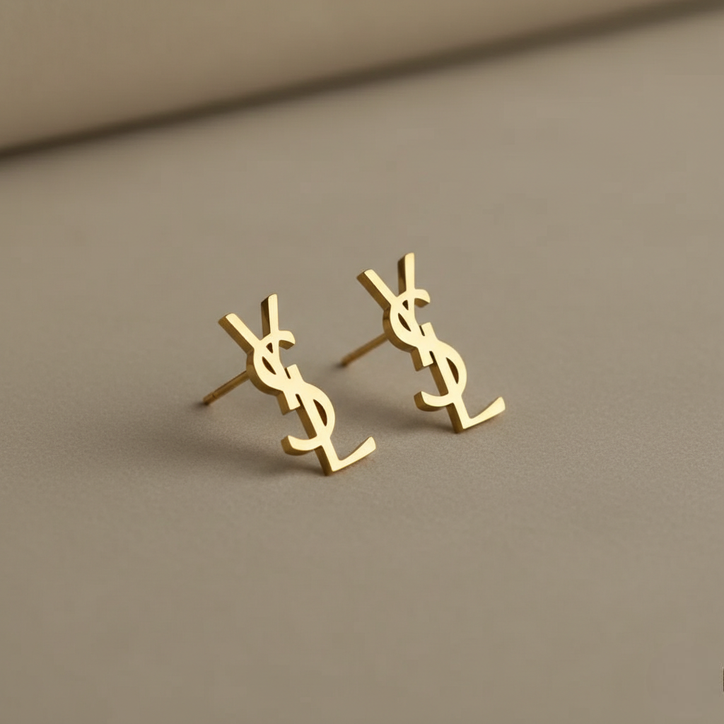 Gold YSL earrings on a beige background