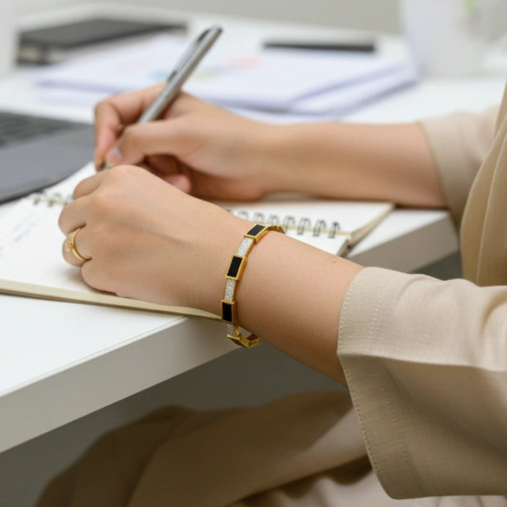 Person writing in a notebook with a pen, wearing a gold bracelet.