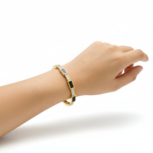 Hand wearing a gold bracelet with black and blue accents on a white background