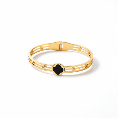 Gold bracelet with a black clover-shaped clasp on a white background