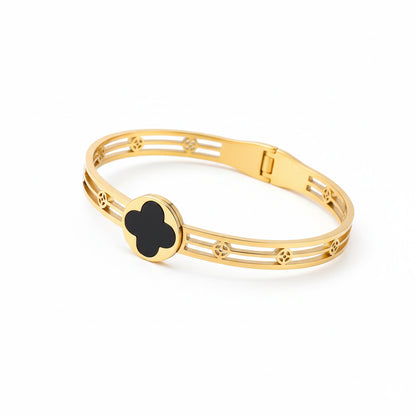 Gold bracelet with a black clover shaped charm on a white background