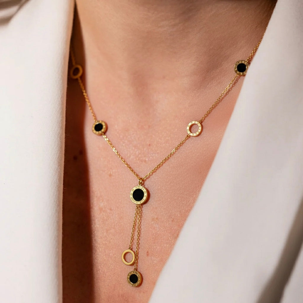 Gold necklace with black stones worn by a person against a white background