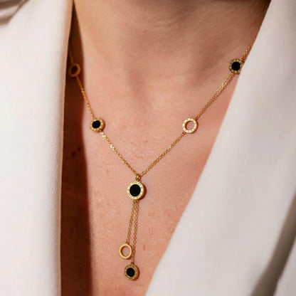 Gold necklace with black stones worn by a person against a white background