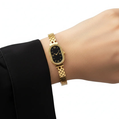 Gold wristwatch on a person's wrist with a black face against a white background