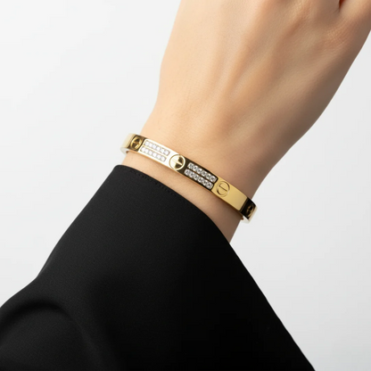 Gold bracelet with brand logo on a wrist against a plain background