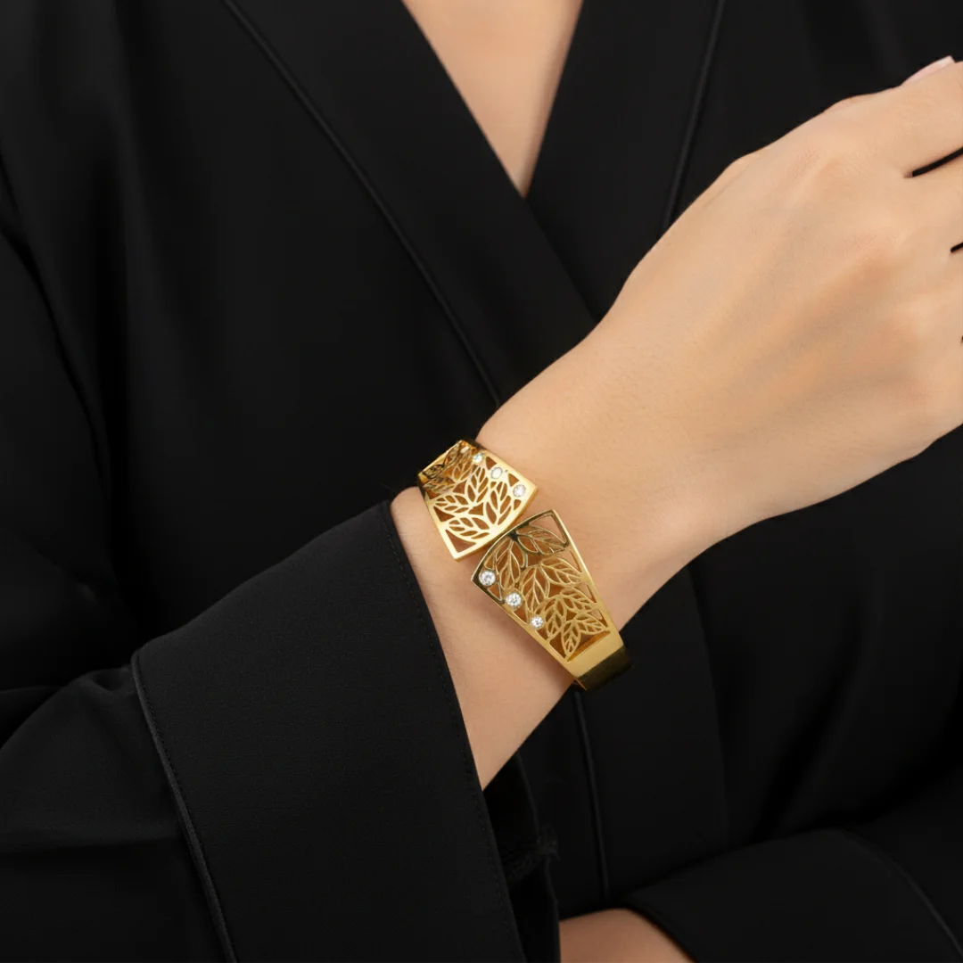 Gold bracelet with intricate design worn on a wrist against a black background