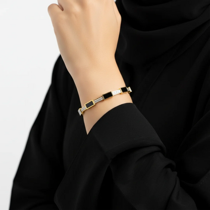 Bracelet with black and gold design on a wrist, wearing a black garment.