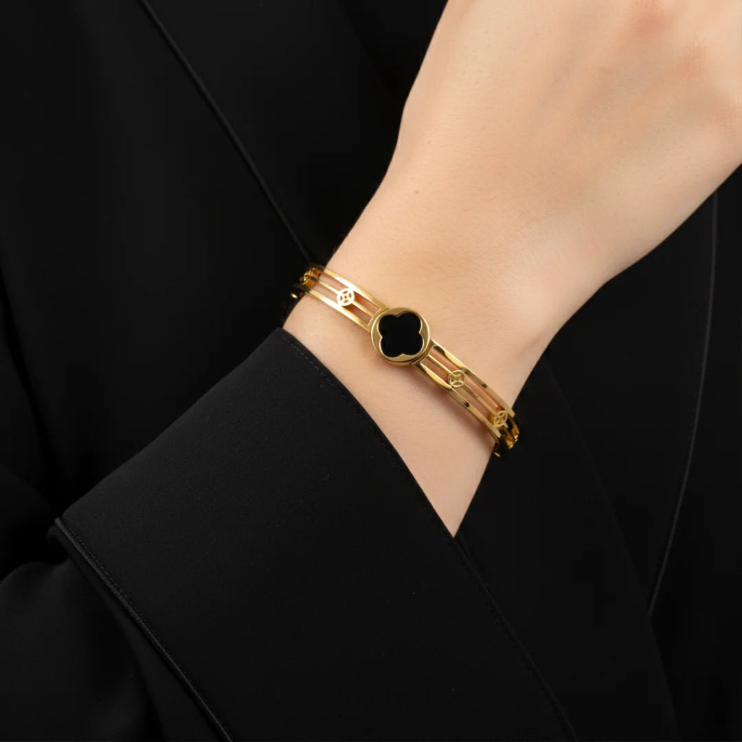 Gold bracelet with a black heart charm on a person's wrist against a black background