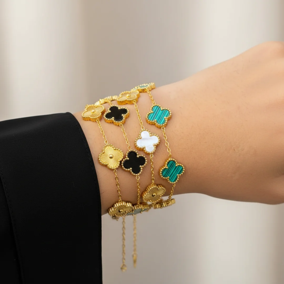 Gold bracelet with clover-shaped charms on a wrist against a neutral background