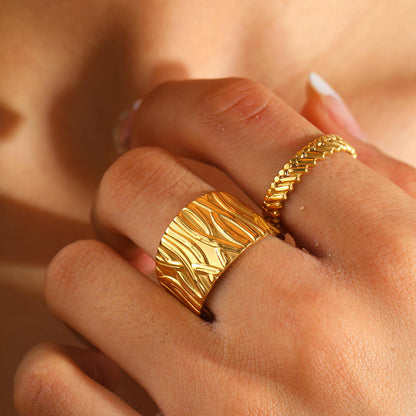 Gold ring with a textured design worn on a finger against a blurred background