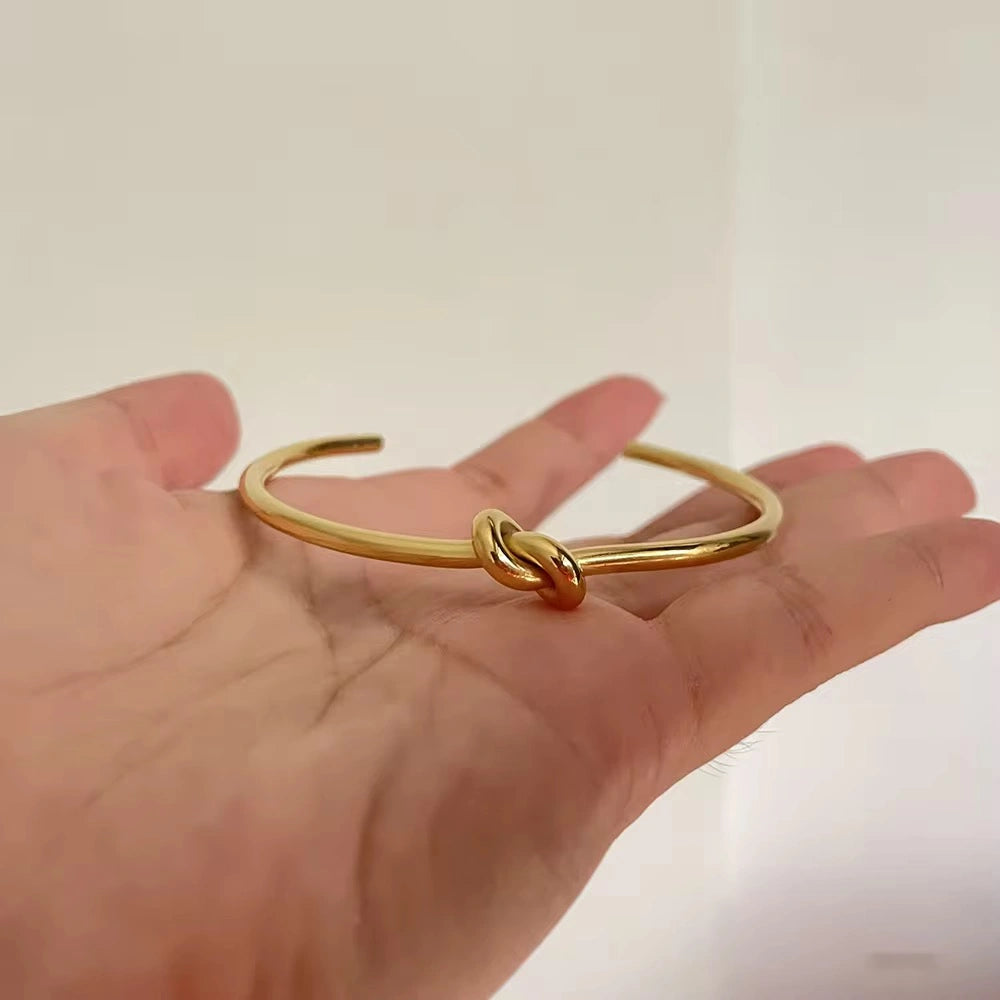 Gold knot bangle on a hand against a plain background