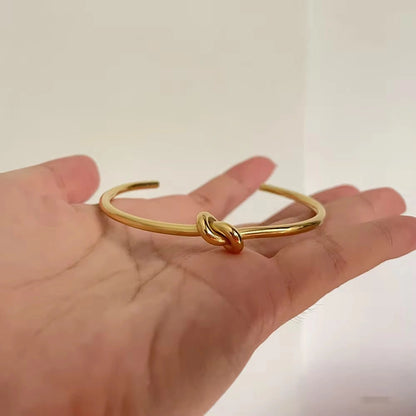 Gold knot bangle on a hand against a plain background