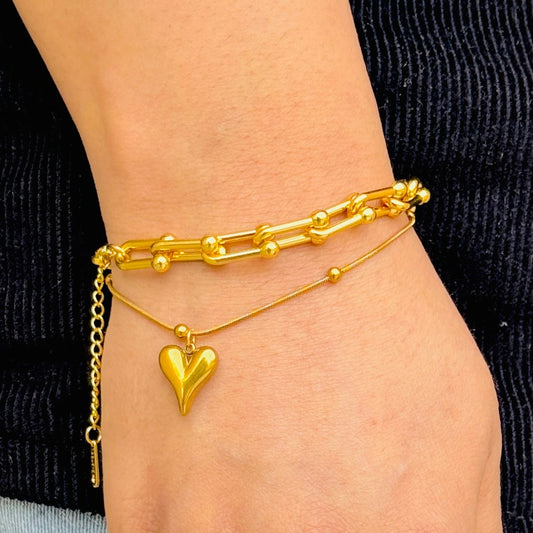 Gold anklets on a person's ankle with a heart-shaped charm.