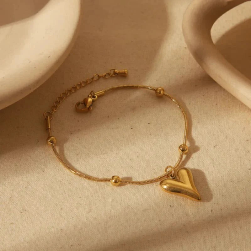 Gold bracelet with a heart charm on a beige surface