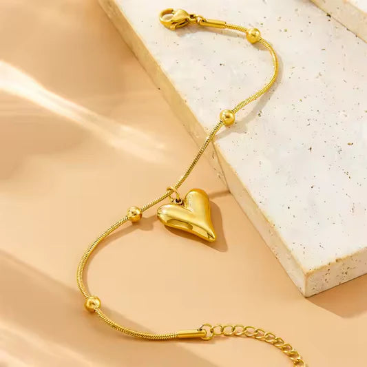 Gold bracelet with a heart-shaped clasp on a beige surface