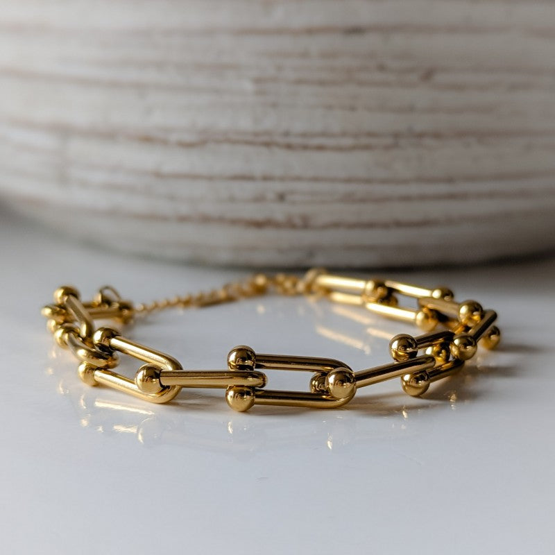 Gold chain bracelet on a white surface with a neutral background