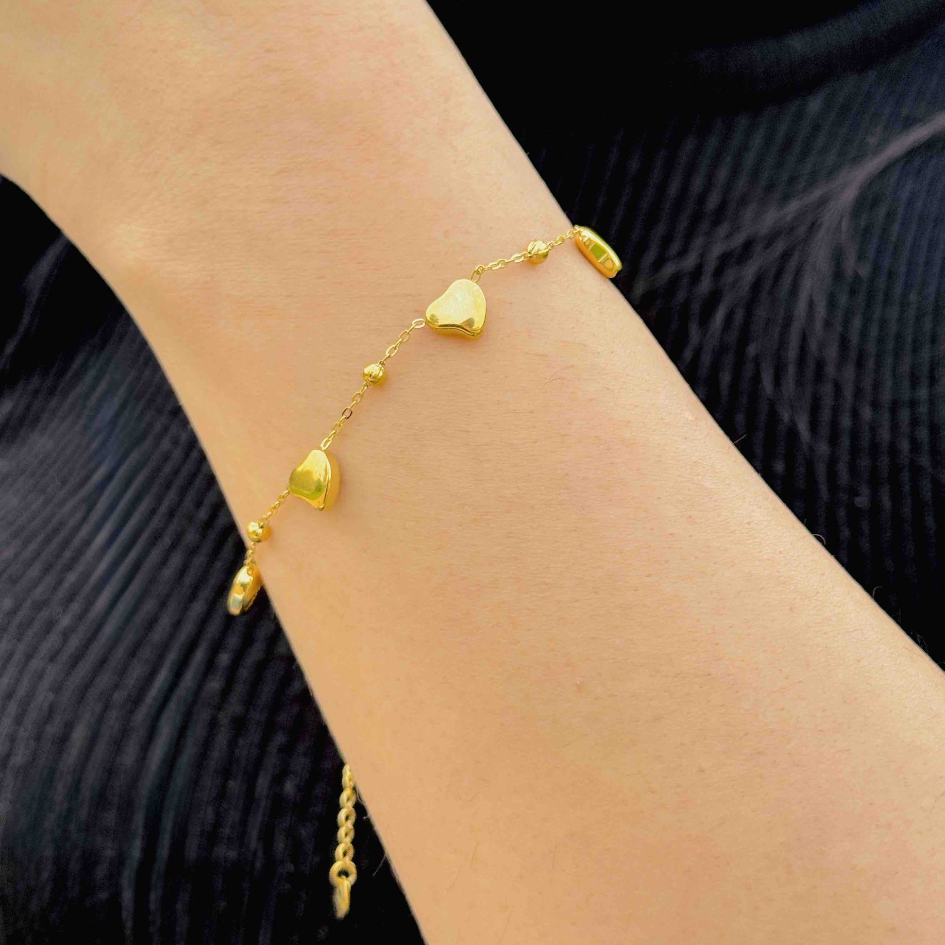 Gold bracelet with heart-shaped charms on a wrist against a black background