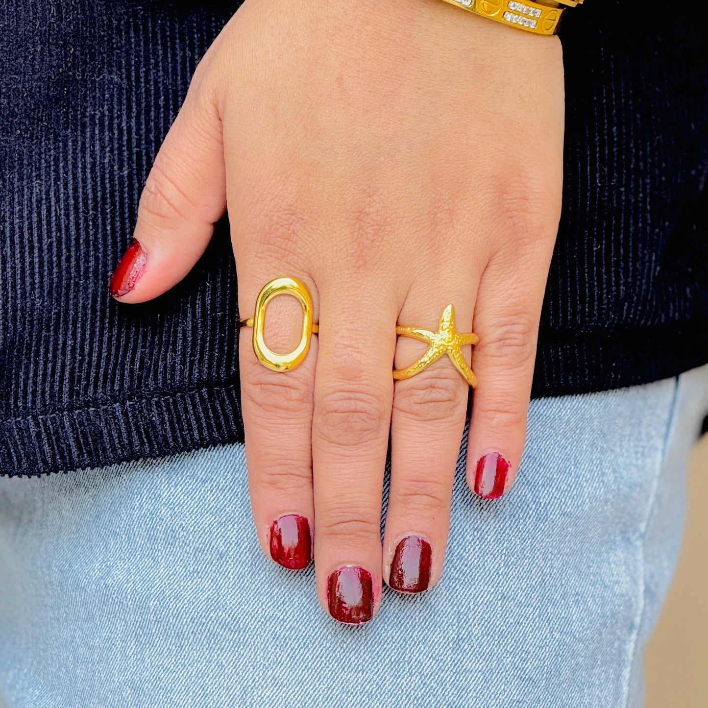 Hand wearing two gold rings with red nail polish on a dark background
